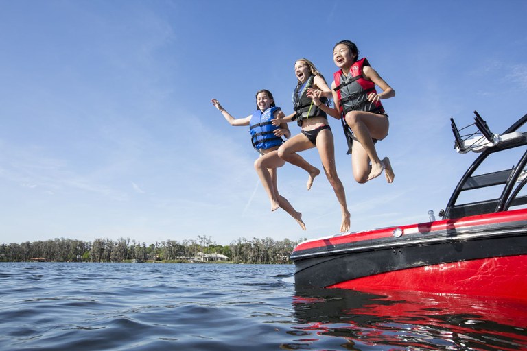 3 girls wearing life jackets jumping from a boat